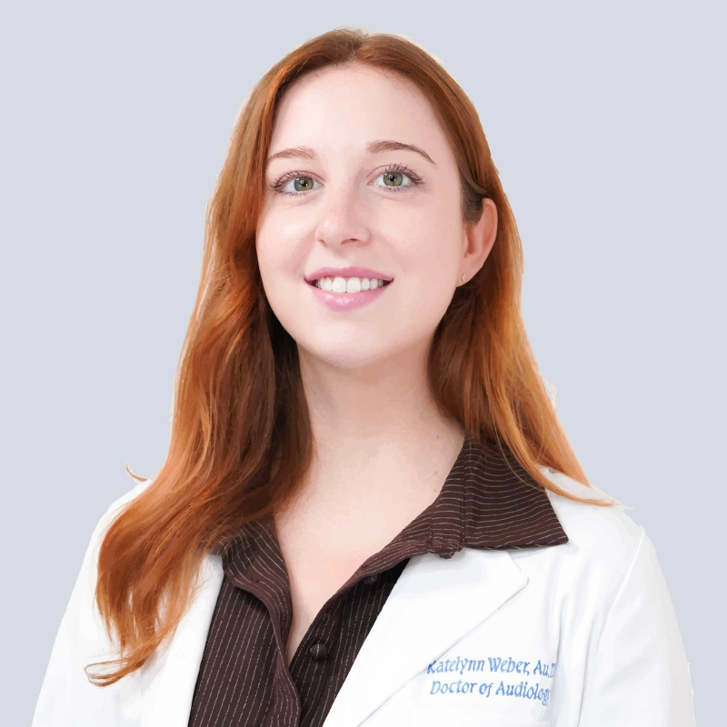 Smiling red-haired woman in a white lab coat and dark blouse, posed against a light gray background